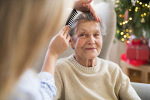 A Health Visitor Combing Hair Of Senior Woman At Home At Christmas