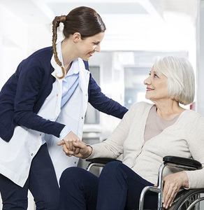 A nursing home nurse smiling at a patient in a wheelchair