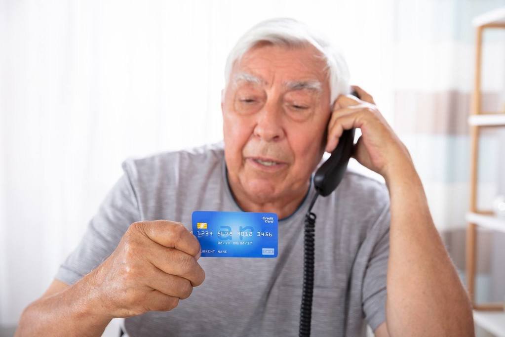A senior citizen on the phone holding a credit card avoiding financial fraud