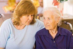 A concerned looking lady with an elderly person in a wheelchair inside a nursing home.