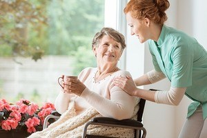 A professional caretaker in uniform helping an elderly women in a wheelchair at a nursing home