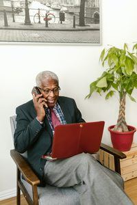 older man on the phone while working on a computer