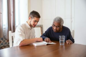 nursing home aide helping an elderly man read a book