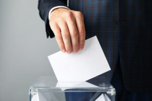 Man putting ballot into voting box against gray background